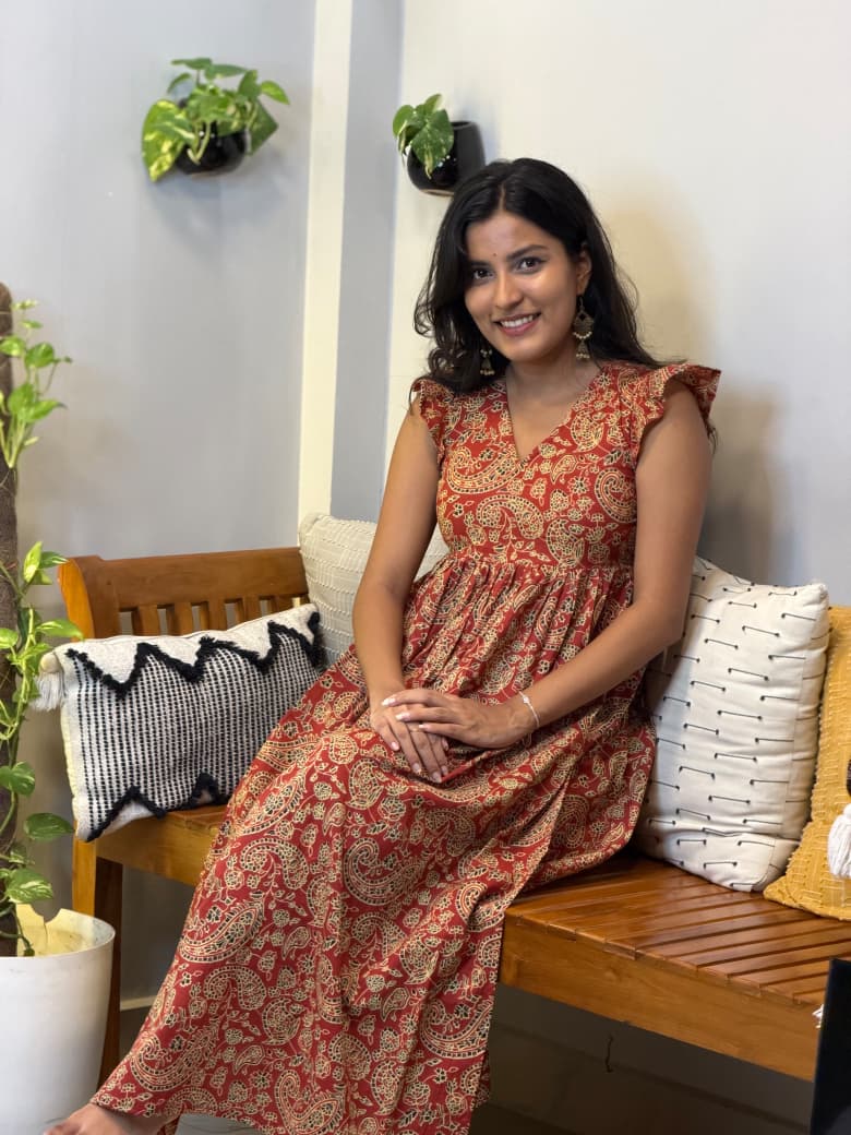 [PBC1036] Rust Paisley Hand-Block Jaipur Soft Cotton – model seated on bench showing full dress length and paisley print