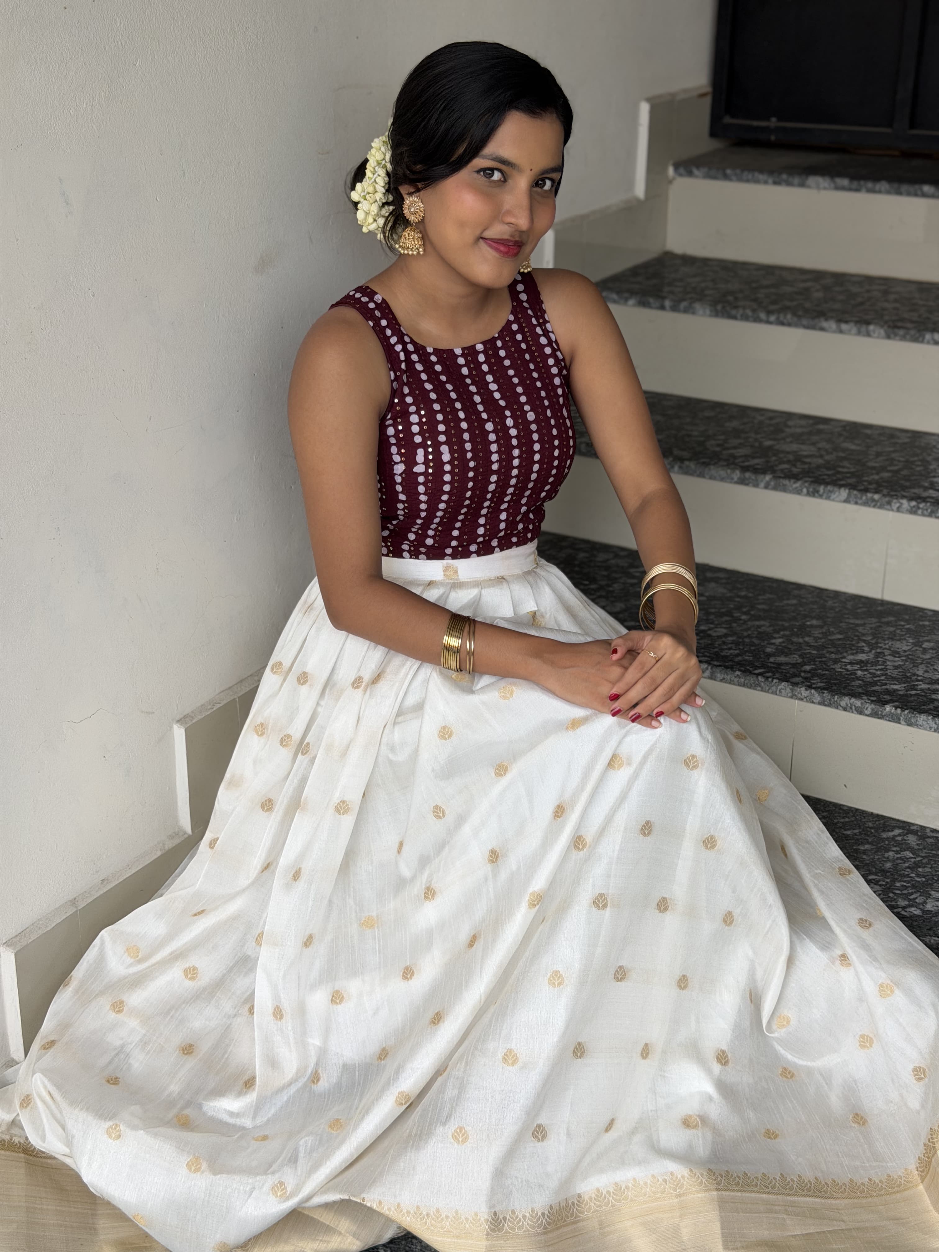 [PBC1071] Maroon bandhani blouse with ivory Kasavu skirt – full-length seated view